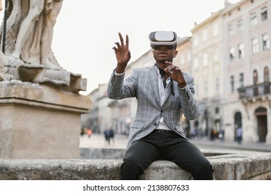 Handsome african american man wearing VR headset while sitting on old fountain outdoors. Successful male entrepreneur using modern innovation for work. - Powered by Shutterstock