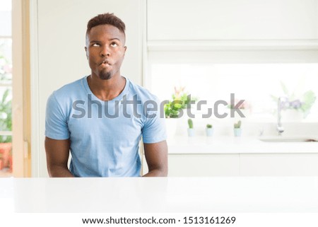 Handsome african american man wearing casual t-shirt at home making fish face with lips, crazy and comical gesture. Funny expression.