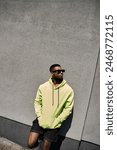 Handsome African American man in a yellow hoodie leans against a wall.