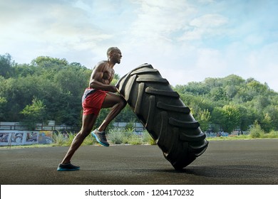 Handsome african american muscular man flipping big tire outdoor. - Powered by Shutterstock