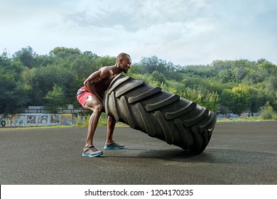 Handsome african american muscular man flipping big tire outdoor. - Powered by Shutterstock