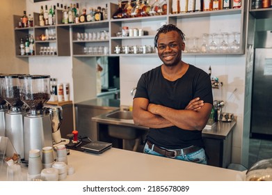 Handsome African American Small Coffee Shop Owner Standing Behind Counter Whit His Arms Crossed. Black Barista Working During A Day. Portrait Of A Successful Businessman.