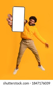 Handsome African American Young Man Recommending New Mobile Application, Collage. Excited Black Guy Holding Smartphone, Showing Blank Screen, Jumping Up Over Orange Studio Background