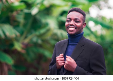 Handsome African Business Man Standing In Trendy Formal Black Suit. Guy With Beard Wearing Blue Long Sleeve Or Sweater