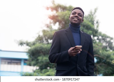 Handsome African Business Man Using Smartphone In Trendy Formal Black Suit. Guy With Beard Wearing Blue Long Sleeve Or Sweater