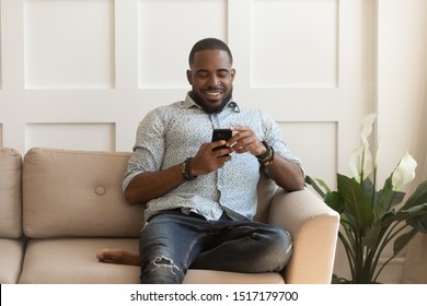 Handsome african guy sitting on couch chatting with girlfriend using smartphone sharing instant messages, e-dating active user, e-commerce customer buying online, internet amusements new apps concept