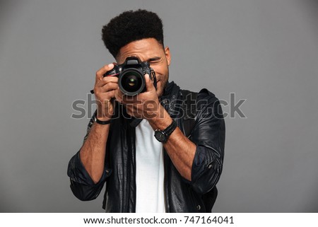 Handsome african guy with stylish haircut taking photo on digital camera, isolated on gray background