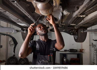 Handsome African Male Repairing Bottom Of Car, Check And Examine All Details. Hardworking Man In Uniform At Work