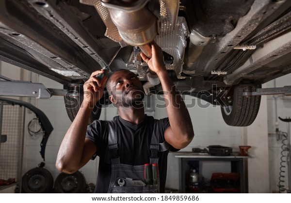 handsome\
african male repairing bottom of car, check and examine all\
details. hardworking man in uniform at\
work