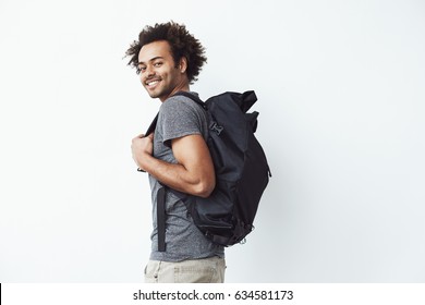 Handsome african man with backpack smiling standing against white wall ready to go hiking or a student on his way to university.