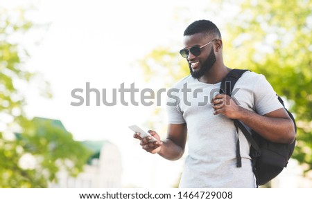 Handsome african man with backpack textmessaging on phone and smiling, panorama, copy space