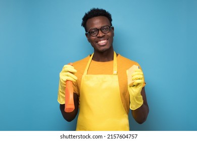 Handsome African Man From Cleaning Service Ready For Tidying Up Your Apartment With Detergent And Sponge. Studio Shot On Blue Wall