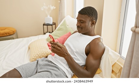 Handsome african man relaxing in a cozy bedroom using red smartphone, radiating modern home comfort - Powered by Shutterstock