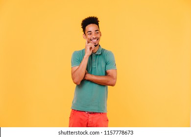 Handsome African Man Thinking About Something With Smile. Indoor Shot Of Positive Black Guy Expressing Good Emotions On Bright Background.