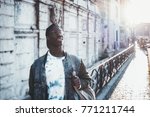 Handsome African student boy in a jean jacket and round glasses is looking upside while standing outdoor; male black undergraduate young guy on his way to university with copy space place for text