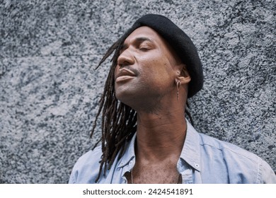 handsome African-American man in braids with stylish beret looking away while standing against grey wall and eyes closed - Powered by Shutterstock
