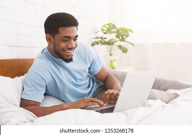 Handsome african-american man lying in bed and watching something on laptop, copy space - Powered by Shutterstock