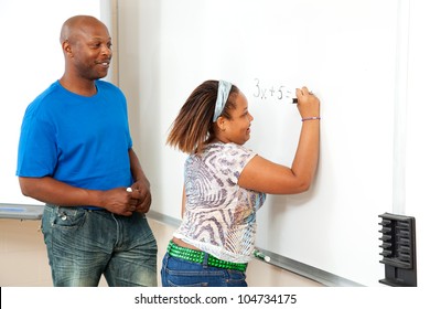 Handsome African-american Math Teacher Works With A Student At The Board.