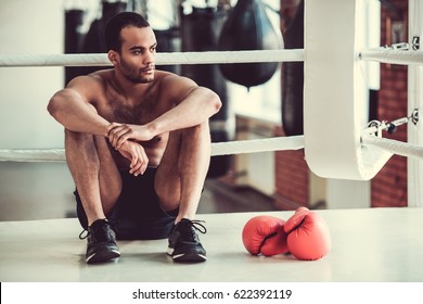 Handsome Afro American boxer with bare torso is looking away while sitting on the boxing ring - Powered by Shutterstock