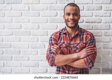 Handsome Afro American man is looking at camera and smiling, standing with crossed arms against white brick wall - Shutterstock ID 2224876665