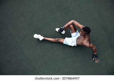 Handsome Afro American Runner Sitting On The Street While Taking Break After Training. Black Male Runner Having Rest After Workout