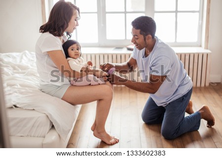 handsome afro guy putting on socks on his baby's feet, child care. full length side view photo