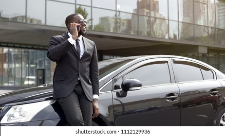 Handsome Afro-American man talking on phone with smile on face near office