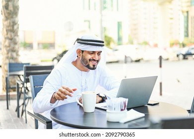 Handsome Arab Emirati Man In A Kandora Using Laptop And Drinking Coffee