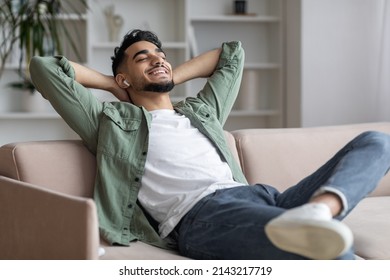Handsome Arab Guy In Airpods Easrphones Listening Music At Home, Smiling Middle Eastern Man Leaning Back On Couch With Closed Eyes And Hands Behind Head, Enjoying Favorite Playlist, Closeup