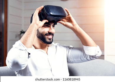 Handsome Arab Man Uses Black VR Goggles Set Sitting On The Sofa In Home Studio