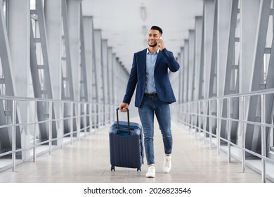 Handsome Arab Man Walking With Suitcase In Airport And Talking On Cellphone, Young Middle Eastern Businessman Booking Transfer By Phone After Arrival, Enjoying Pleasant Conversation, Copy Space