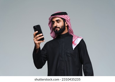 Handsome arab middle-eastern saudi arabian man with traditional saudi clothing in studio - Arabic muslim adult male businessman wearing thwab portrait isolated on gray background
