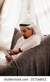 Handsome Arabian Male Sitting On Sofa And Using Digital Tablet