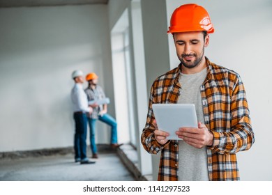 handsome architect in plaid shirt and hard hat standing inside of building house and using tablet - Shutterstock ID 1141297523