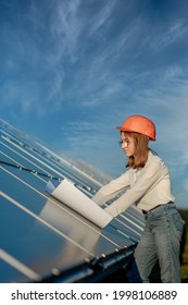 Handsome Architect Woman Examining A Draft Map Or Blueprint Project Plan, Worker Activity Looking Out In Photovoltaic Cell Farm Or Solar Panels Field.