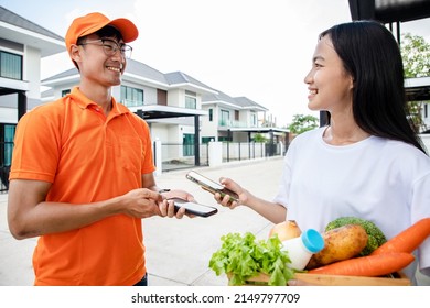 Handsome Asian Delivery Man In An Orange Uniform Holds Smartphone For Using QR Code Scan Payment Customers For An Online Order. Domestic And International Transport And Logistics