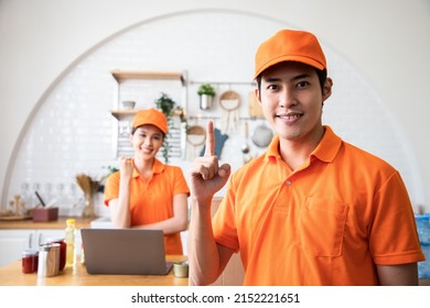 Handsome Asian Delivery Man In An Orange Uniform Hands Up For Show Number One To Build Confidence For Cook Customers In Kitchen. Domestic And International Transport And Logistics