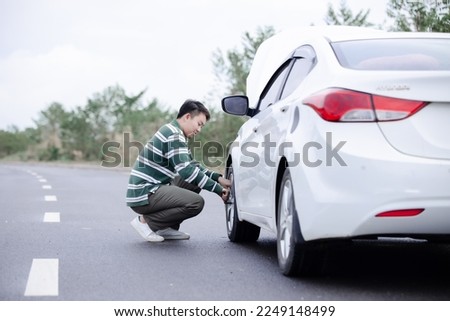 Handsome Asian man checking the punctured tyre on his car loosening the nuts with a wheel spanner before jacking up the vehicle in street. Men hold rubber to repair. Change tire. broken car concept.