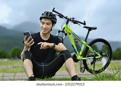 Handsome asian man cyclist taking a break resting from cycling bike in the morning and using mobile phone - Powered by Shutterstock