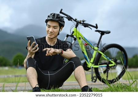 Handsome asian man cyclist taking a break resting from cycling bike in the morning and using mobile phone