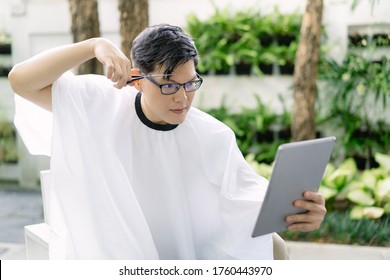 Handsome Asian Man Having His Hair Cut And Looks In The Mirror At Home During The Coronavirus Pandemic, Self Hair Care During Quarantine.