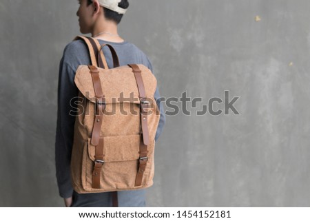 Handsome Asian man with lightbrown ( cork ) canvas backpack smiling standing with cap.