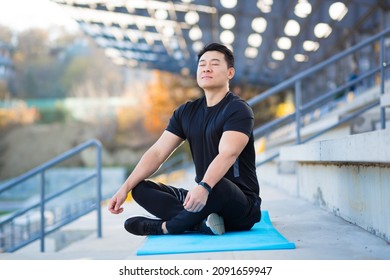 Handsome Asian Man Meditating In Modern Urban Stadium, Sitting Lotus Pose Male Practicing Yoga Mat, Zen. Relaxes Outdoors In Nature In The Morning Concept Healthy Lifestyle, Relax, Calm, Meditation