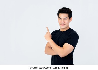 Handsome Asian Man In Plain Black T-shirt Smiling And Pointing Hand Upward To Empty Space Isolated On White Background