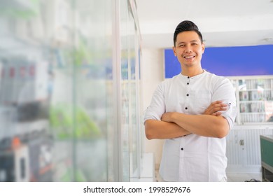handsome asian man smiling with crossed hands while standing near cell phone accessories display case in cell phone shop