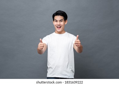 Schöner asiatischer Mann, der lächelt und Daumen auf grauem Hintergrund aufgibt
