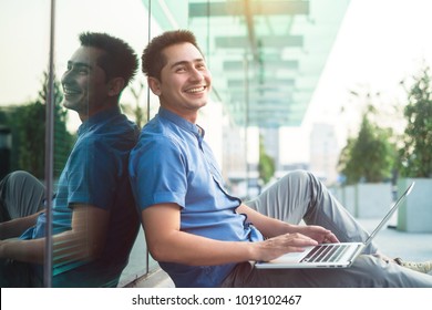 Handsome Asian Man Using Laptop And Looking Something Happily With His Smile Outside Office In The Evening.