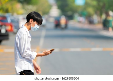 Handsome Asian Man Using Smartphone Walking In The City Street. Protection Against Flu, Pollution And Contagious Diseases. Copy Space