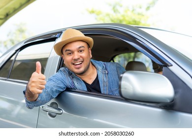 Handsome Asian Man Wear Hat The Blue Jeen Shirt Is Driving And Thumbs Up Sitting On Car Seat Showing Thumb Up And Fastening Seat Belt. Car Safety, Insurance, Buying And Selling Cars, Travel Concept.