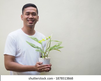 A handsome Asian man wearing blank white shirt smiling while holding plant in a pot isolated on white. Space for text - Powered by Shutterstock